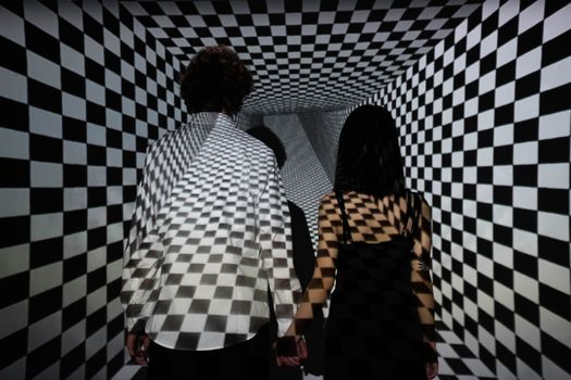 Couple walking in a checkerboard tunnel, creating an optical illusion of depth and connection.
